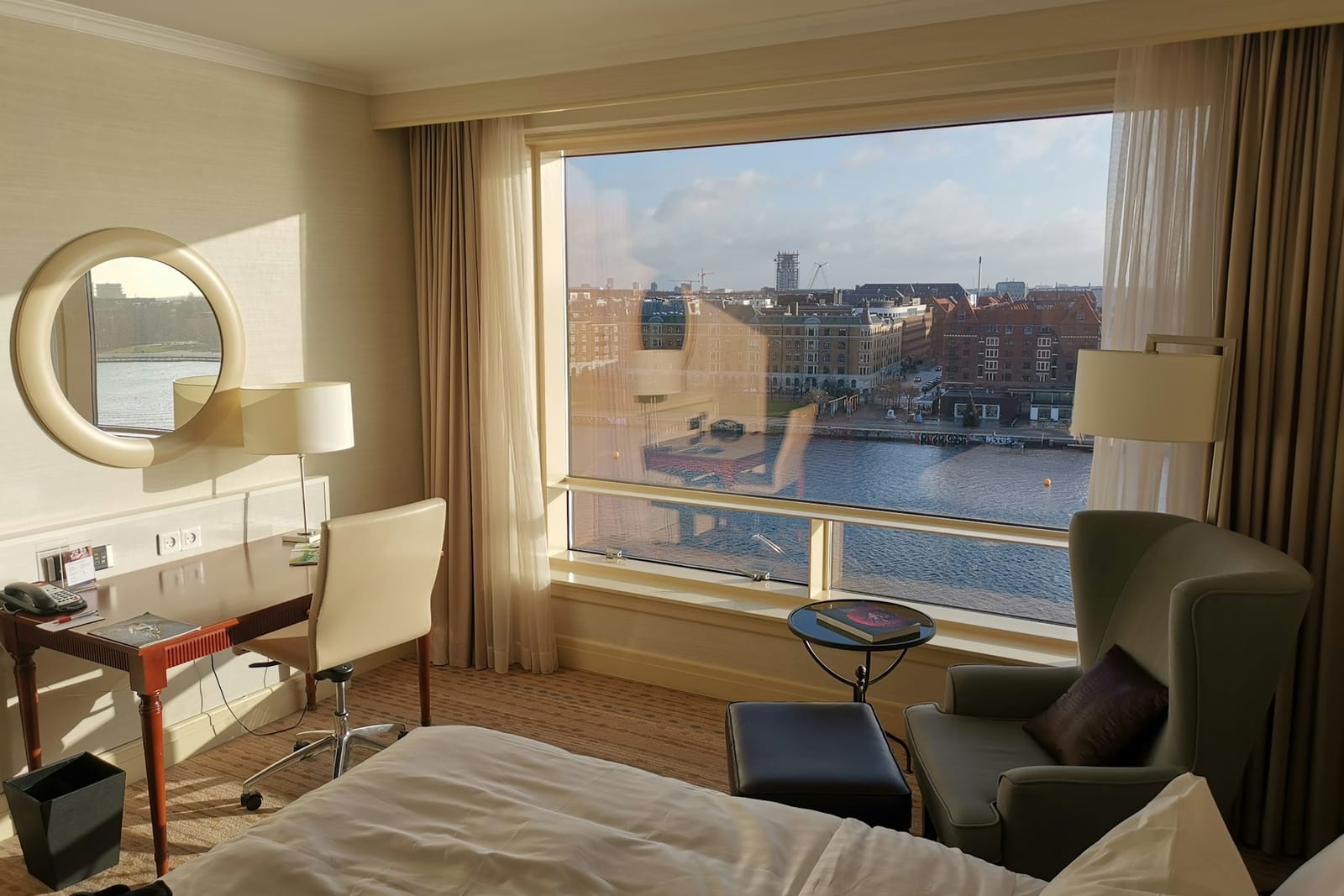 Hotel room with a made bed beside a large window looking over a city